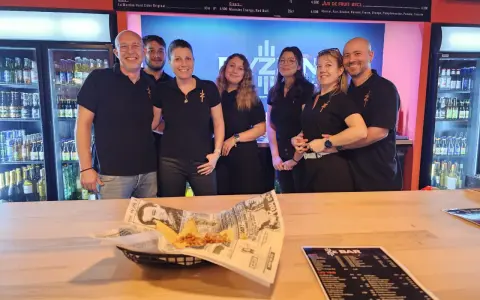 L'équipe du bar Elyzion, souriante, pose devant les réfrigérateurs. Sur le comptoir, des nachos et un menu.
