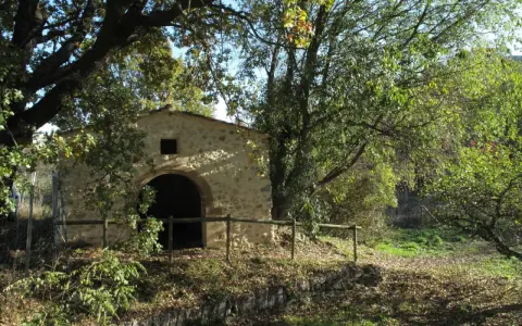 Ancienne bâtisse en pierre avec une arche, entourée d'arbres feuillus et d'une clôture en bois. Un lieu paisible dans le parc de l'arbousière.