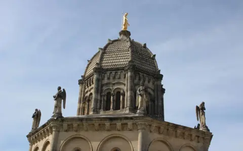 Dôme de Notre Dame de Provence, orné de statues d'anges et surmonté d'une Vierge dorée, sous un ciel bleu.