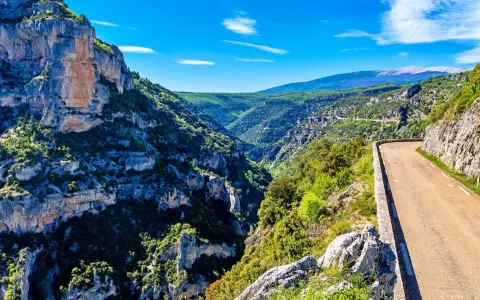 Vue panoramique des gorges de la Nesque, une route sinueuse longeant des falaises abruptes et une végétation luxuriante. Parfait pour une randonnée mémorable.