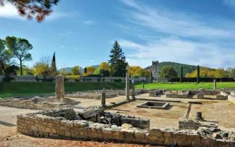 Vestiges romains ensoleillés, parfaits pour visiter Vaison-la-Romaine. Ruines antiques, colonnes et un clocher médiéval en arrière-plan.