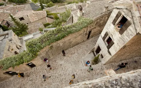 Vue plongeante d'une ruelle pavée bordée de maisons anciennes. Des touristes explorent ce village pittoresque, un peu comme un scad Lacoste, profitant de l'atmosphère paisible.