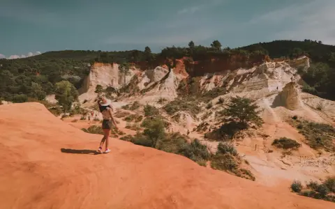 Une femme au chapeau admire le paysage spectaculaire de la carrière d'ocre du Vaucluse, avec ses falaises colorées et sa végétation luxuriante.