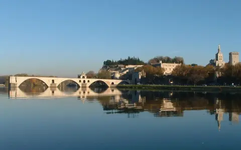 Le pont d'Avignon se reflète dans le Rhône, avec le Palais des Papes et l'île de la Barthelasse en arrière-plan.