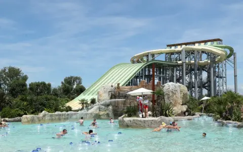 Ambiance estivale dans un parc aquatique Vaucluse. Des familles profitent de la piscine à bouées, sous les imposants toboggans verts et blancs.