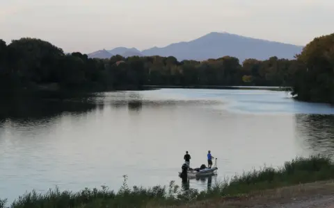Deux pêcheurs sur un bateau profitent du calme du plan d'eau du Revestidou, avec des montagnes en arrière-plan.