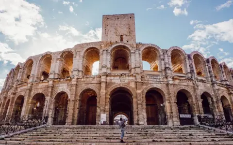 Visiter Arles : une personne tient un bébé sur les marches de l'amphithéâtre romain, sous un ciel bleu et nuageux.