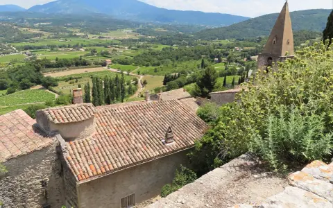 Vue panoramique d'un village provençal avec ses toits de tuiles, sa campagne verdoyante et ses montagnes. Une belle activité gratuite Vaucluse pour s'évader.