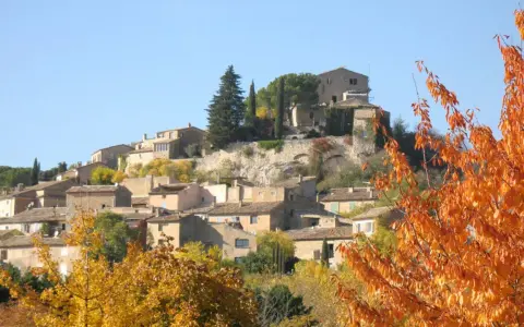 Village de Joucas, France, en automne. Les maisons en pierre s'étagent sur la colline, entourées d'arbres aux couleurs flamboyantes.