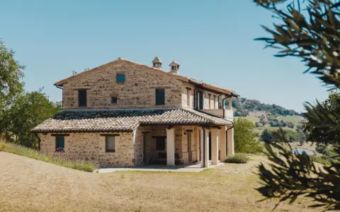 Un mas en pierre typique du sud de la France, niché dans des collines verdoyantes sous un ciel bleu éclatant.