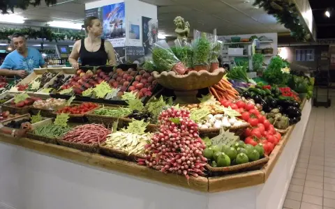 Un étal coloré au marché d'Avignon présente une abondance de fruits et légumes frais : pêches, tomates, haricots verts, radis, aubergines, et plus encore.