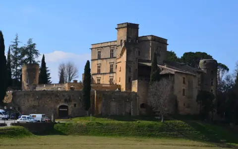 Le majestueux **Château de Lourmarin** se dresse sur une colline, ses pierres ocres baignées de soleil sous un ciel bleu. Des cyprès élancés l'entourent.