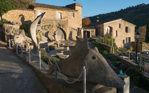 Sculptures étranges devant le musée extraordinaire Ansouis. Un chemin serpente entre des créatures de pierre et des bâtiments en pierre.