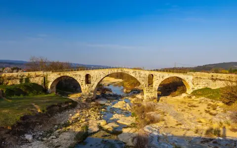 Le **pont Julien**, un ancien pont de pierre à trois arches, enjambe une rivière asséchée bordée de rochers et de végétation.
