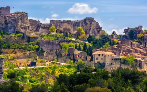 Vue panoramique de la route des villages perchés, avec un château en ruines dominant des maisons en pierre et une végétation luxuriante sous un ciel bleu.
