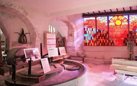 Dans le musée du vitrail Gordes, une roue de moulin ancienne côtoie un vitrail éclatant de soleil et de couleurs chaudes.