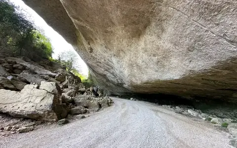 Le chemin menant au fort de Buoux serpente sous un immense surplomb rocheux, offrant un aperçu de la nature sauvage.