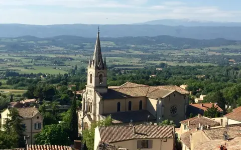 Vue panoramique sur Bonnieux, France, avec son église et ses toits de tuiles, dominant une vallée verdoyante.