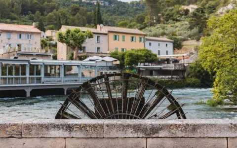 Roue à aubes rouillée sur la Sorgue, avec des maisons provençales en arrière-plan. Le **gouffre de Fontaine-de-Vaucluse** est une source d'eau d'une beauté saisissante.