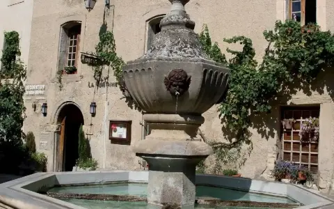 Fontaine en pierre avec des têtes de gargouilles à Venasque, Vaucluse. L'eau coule doucement dans le bassin, entouré de végétation luxuriante.