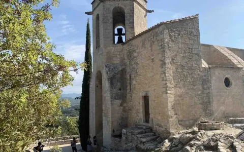 Le clocher de Notre-Dame d'Alidon, avec sa cloche visible, se dresse fièrement sous un ciel bleu. Des visiteurs admirent le paysage.