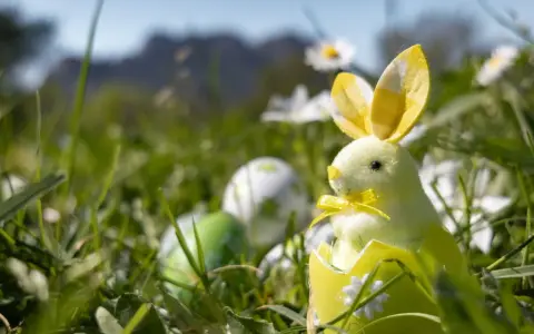 Un adorable lapin de Pâques jaune sort d'un œuf décoré, entouré d'herbe et d'œufs colorés. Idéal pour savoir que faire à Pâques.