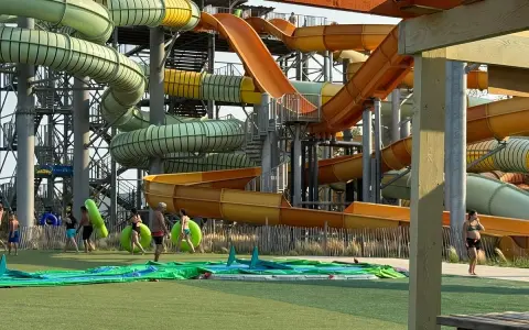 Des toboggans colorés et sinueux dominent le parc aquatique de Monteux. Des visiteurs se préparent à glisser, certains portant des bouées vertes.