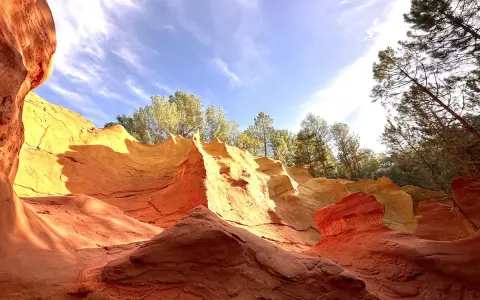 Carrières d'ocre aux couleurs vives, rappelant l'usine d'ocre Mathieu. Le ciel bleu et les arbres verts contrastent avec les roches rouges et jaunes.