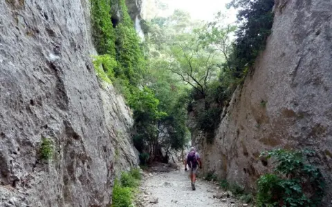 Un randonneur explore les **gorges du Régalon**, un sentier rocailleux bordé de falaises abruptes et de végétation luxuriante.