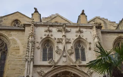 Détail architectural d'une cathédrale, un joyau du tourisme à Carpentras. Gargouilles et fenêtres gothiques sous un ciel couvert.