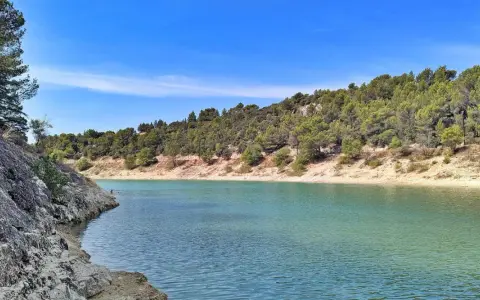 Le lac du Paty, aux eaux turquoise, est bordé de rochers et de collines verdoyantes sous un ciel bleu.