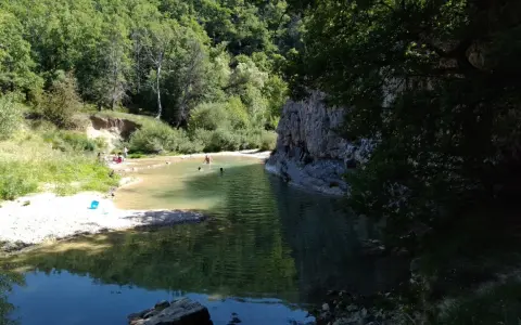 Des baigneurs profitent d'une rivière aux eaux claires près du rocher des abeilles, certains escaladent la paroi rocheuse.