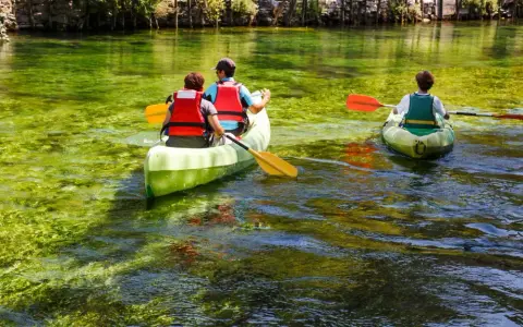 Trois personnes en canoë sur la Sorgue, profitant d'une balade paisible à L'Isle-sur-la-Sorgue. L'eau cristalline révèle la végétation sous-marine.