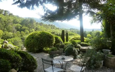Le jardin de la louve, un havre de paix verdoyant avec une table et des chaises invitant à la détente, surplombe une vallée luxuriante.