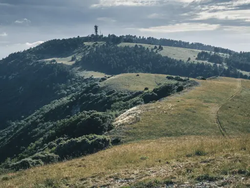 Vue panoramique du Moure Negre, avec une tour de télécommunication au sommet, des collines verdoyantes et un sentier sinueux.