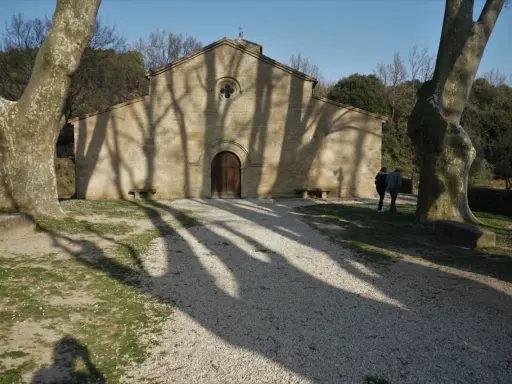L'église de Vaugines, baignée de soleil, accueille deux visiteurs. Les ombres des arbres dansent sur sa façade de pierre.