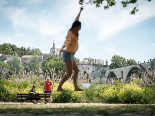 Amusez-vous à Avignon ce week-end ! Une jeune femme saute devant le Palais des Papes et le Pont d'Avignon.