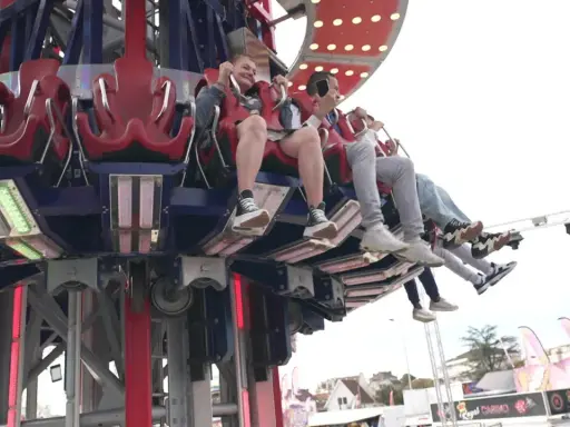 Des jeunes s'amusent dans une attraction de la fete foraine 84, leurs pieds balançant dans le vide.