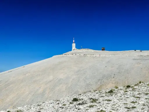 Le Mont Ventoux, sommet aride sous un ciel bleu intense, dominé par une tour de télécommunication.