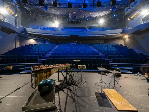Scène de concert vide avec sièges bleus, marimba, batterie et projecteur, prête pour un spectacle à la Scala Provence.
