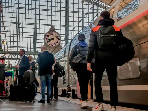 Voyageurs attendant le train pour Apt, sous une grande horloge dans une gare.