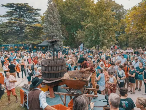 Foule joyeuse à Avignon pour le ban des vendanges, avec un pressoir à vin traditionnel au centre.