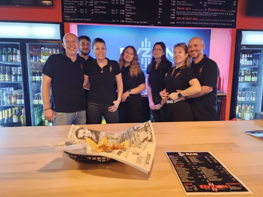 L'équipe du bar Elyzion, souriante, pose devant les réfrigérateurs. Sur le comptoir, des nachos et un menu.