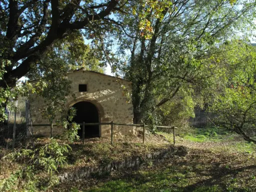 Ancienne bâtisse en pierre avec une arche, entourée d'arbres feuillus et d'une clôture en bois. Un lieu paisible dans le parc de l'arbousière.