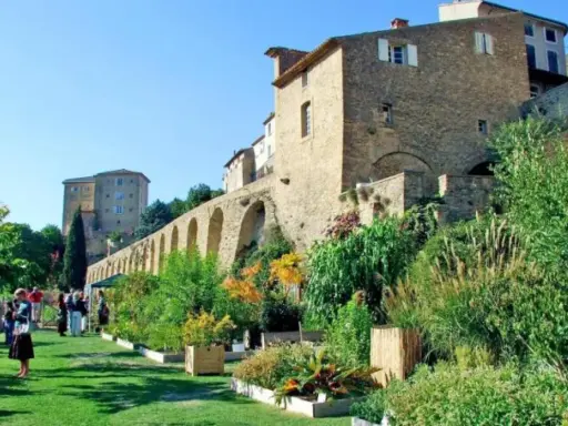 Jardin luxuriant devant le **château de Lauris**, avec ses murs de pierre et ses arches médiévales.