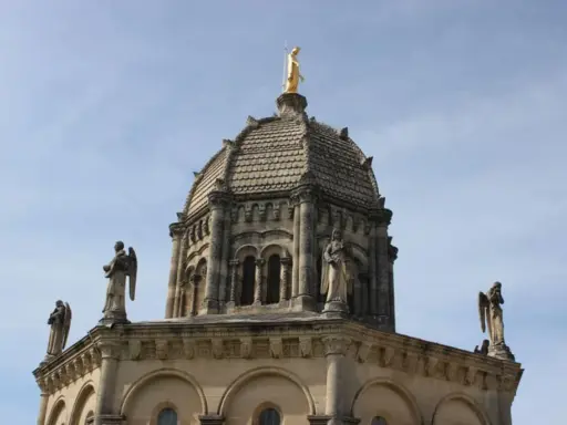 Dôme de Notre Dame de Provence, orné de statues d'anges et surmonté d'une Vierge dorée, sous un ciel bleu.