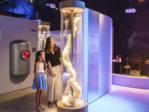Une mère et sa fille découvrent la filaventure dans un musée interactif, fascinées par une colonne de fibres.