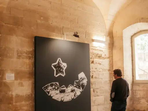 Un homme admire une œuvre d'art abstraite lors d'une expo Avignon. La pièce représente une étoile au-dessus d'une forme souriante composée de fragments.