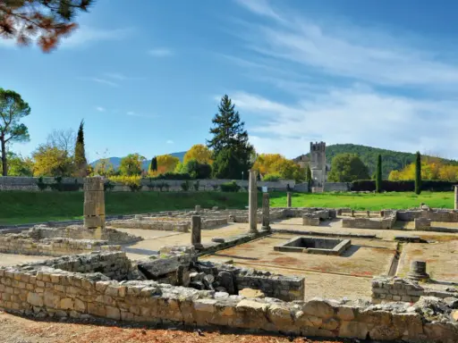 Vestiges romains ensoleillés, parfaits pour visiter Vaison-la-Romaine. Ruines antiques, colonnes et un clocher médiéval en arrière-plan.