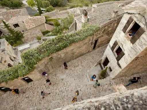 Vue plongeante d'une ruelle pavée bordée de maisons anciennes. Des touristes explorent ce village pittoresque, un peu comme un scad Lacoste, profitant de l'atmosphère paisible.